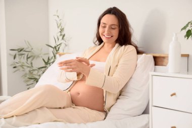 Genç hamile kadın yatak odasında el kremi sürüyor.