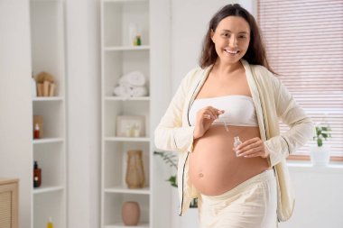 Genç hamile kadın banyoda kozmetik serumu uyguluyor.