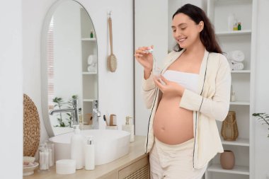 Banyoda kozmetik serumlu hamile bir kadın var.