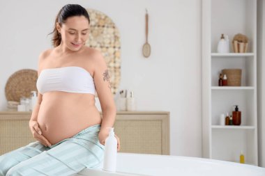 Genç hamile kadın banyoda vücut losyonu sürüyor.