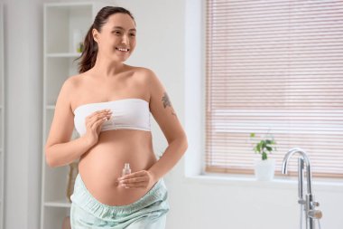 Banyoda kozmetik serumlu hamile bir kadın var.