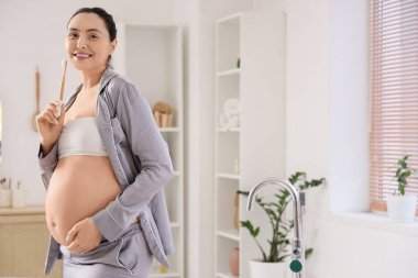 Banyoda diş fırçasıyla hamile bir kadın.