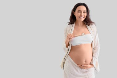 Dişlerini arka planda fırçalayan hamile bir kadın.