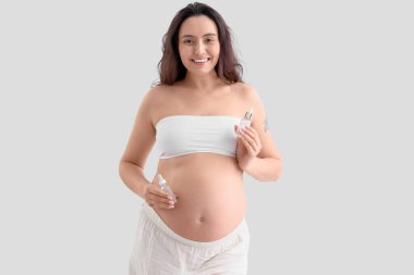 Hafif arka planda kozmetik serumu olan hamile bir kadın.