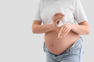 Genç hamile kadın arka plana vücut kremi sürüyor, yakın plan.