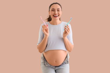 Bej arka planda diş fırçası olan hamile bir kadın.