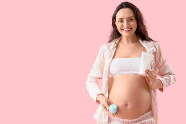 Pembe arka planda vücut kremi ve losyonu olan hamile bir kadın.