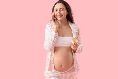 Pembe arka planda yüz kremi olan hamile bir kadın.