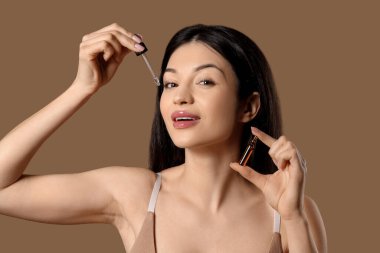 Kahverengi arka planda ampul ve damlatıcısı olan güzel genç bir kadın, yakın plan.