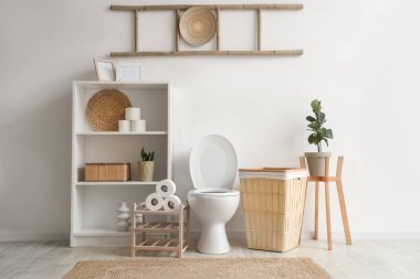 İçinde klozet, raf ünitesi ve sepeti olan ışık tuvaleti.