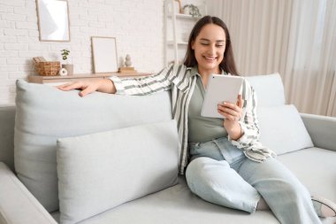 Evdeki koltukta tablet bilgisayar kullanan güzel bir kadın.