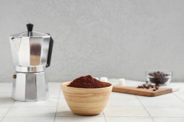 Tahta bir kase kahve tozu ve beyaz fayans üzerinde gayzer kahve makinesi.