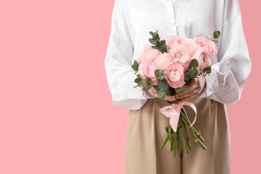 Pembe arka planda bir buket ranunculus çiçeği ve okaliptüs olan genç kadın, yakın plan.