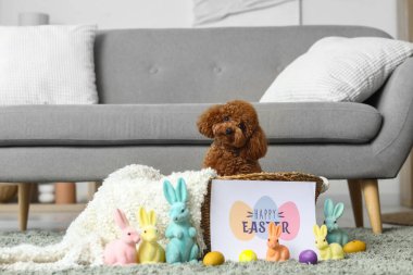 Paskalya yumurtaları, oyuncak tavşanlar ve evde tebrik kartıyla hasır sepette oturan sevimli oyuncak kaniş köpeği.
