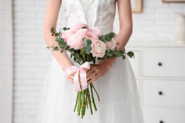 Gelinlik giymiş, evinde bir buket güzel ranunculus çiçeği olan genç bir kadın.