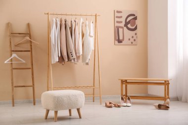 Şık kıyafetler, merdiven, puf ve bankla dolu bir oda.