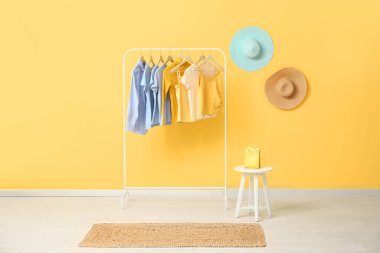 Sarı duvarın yanında asılı giysiler ve alışveriş çantasıyla dizilin.