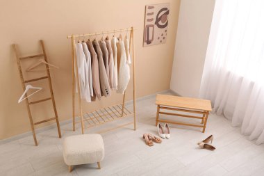 Şık kıyafetler, merdiven, puf ve bankla dolu bir oda.