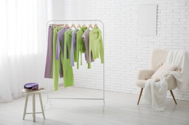 Sallanan giysiler, koltuk ve çanta beyaz tuğla duvarın yanında duruyor.