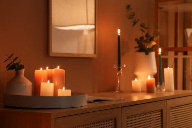 Karanlık odadaki çekmecelerin üzerinde okaliptüslü mumlar ve vazolar yakıyor.