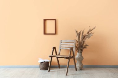 Konforlu ahşap sandalye, vazo dolusu otlar ve turuncu duvarın yanında kitap.