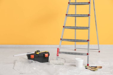 Aletleri ve sarı duvarın yanındaki boya aletleri ile bakım merdiveni