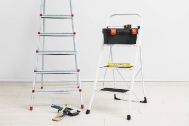 Aletleri ve beyaz duvarın yanında boya aletleri olan bakım merdivenleri
