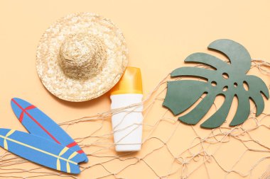 Hasır şapkalı mini sörf tahtaları, güneş kremi ve bej arka planda kağıt tropikal yaprak. Yaz konsepti