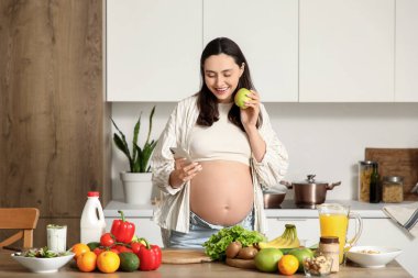 Elmalı hamile bir kadın mutfakta cep telefonu kullanıyor.