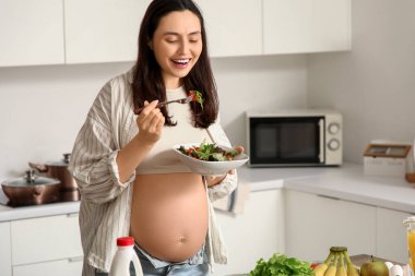 Mutfakta sebze salatası olan hamile bir kadın.