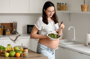 Mutfakta sebze salatası olan hamile bir kadın.