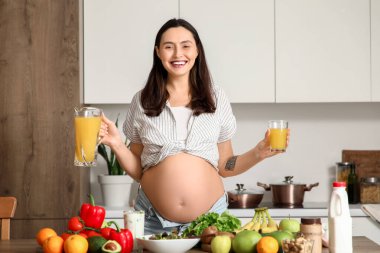 Mutfakta portakal suyu içen hamile bir kadın.