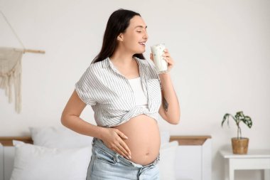 Genç hamile kadın yatak odasında yoğurt içiyor.