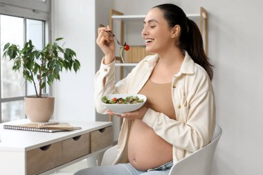 Evdeki masada sebze salatası yiyen hamile bir kadın.