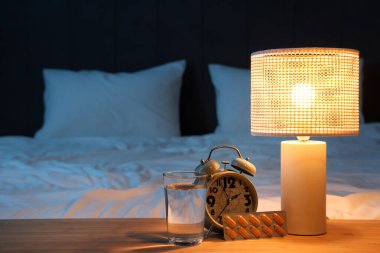 Çalar saat, melatonin hapları, bir bardak su ve geceleri yatak odasındaki masada parlayan lamba.