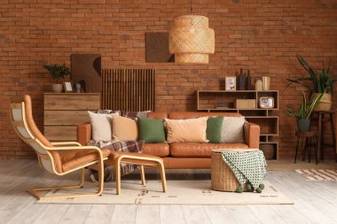 Oturma odasının içinde deri kanepe, koltuk, hasır sepet ve raf ünitesi var.