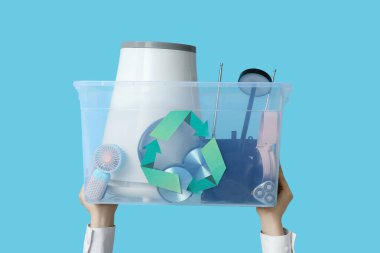 Mavi arka plandaki konteynırda geri dönüşüm için elektronik atığı olan kadın eller