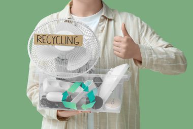 Konteynırda geri dönüşüm için elektronik atığı olan kadın yeşil arka planda başparmağını kaldırıyor