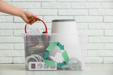 Beyaz tuğla duvarın yanındaki konteynırda geri dönüşüm için elektronik atığı olan kadın el.