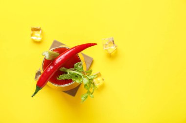 Sarı arka planda kırmızı biberli, kerevizli ve buzlu bir bardak Bloody Mary kokteyli.