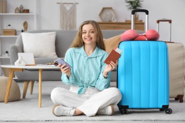 Pasaportlu, cep telefonlu ve bavullu mutlu genç kadın evde oturuyor.