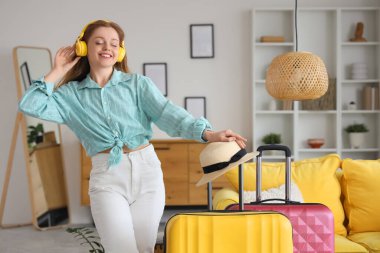 Evde bavulları olan kulaklıklı mutlu genç bir kadın.