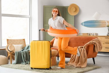 Evinde şişme yüzük ve bavulu olan mutlu genç bir kadın.