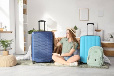 Evinde bavul ve sırt çantalı, yaz şapkalı mutlu genç bir kadın.