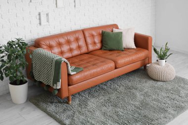 Beyaz tuğla duvarın yanında şık deri kanepe, kanepe ve ev bitkileriyle oturma odasının içinde.