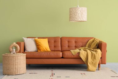 Oturma odasının içinde sehpa sehpası ve yeşil duvarın yanındaki şık deri koltukta yastıklar.