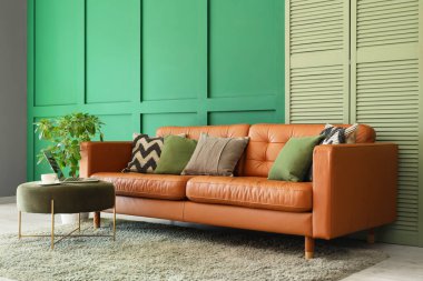 Oturma odasının içinde şık bir deri kanepe, katlanabilir ekran ve yeşil duvarın yanındaki bir laptopta.