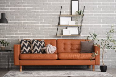 Gri tuğla duvarın yanında ev bitkileri, raflar ve şık deri kanepe olan oturma odasının içinde.