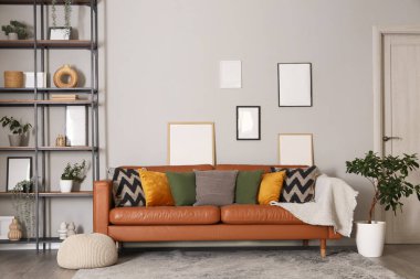 Oturma odasının içinde raf üniteleri, şık deri kanepe, ev bitkileri ve gri duvarlı çerçeveler.