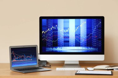 Ofisteki masadaki döviz kurlarının diyagramlarıyla birlikte dizüstü bilgisayar ve bilgisayar monitörü